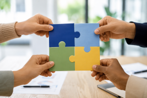 Vier Hände setzen gemeinsam farbige Puzzleteile zusammen als Symbol für Kooperation und gemeinsames Handeln 
